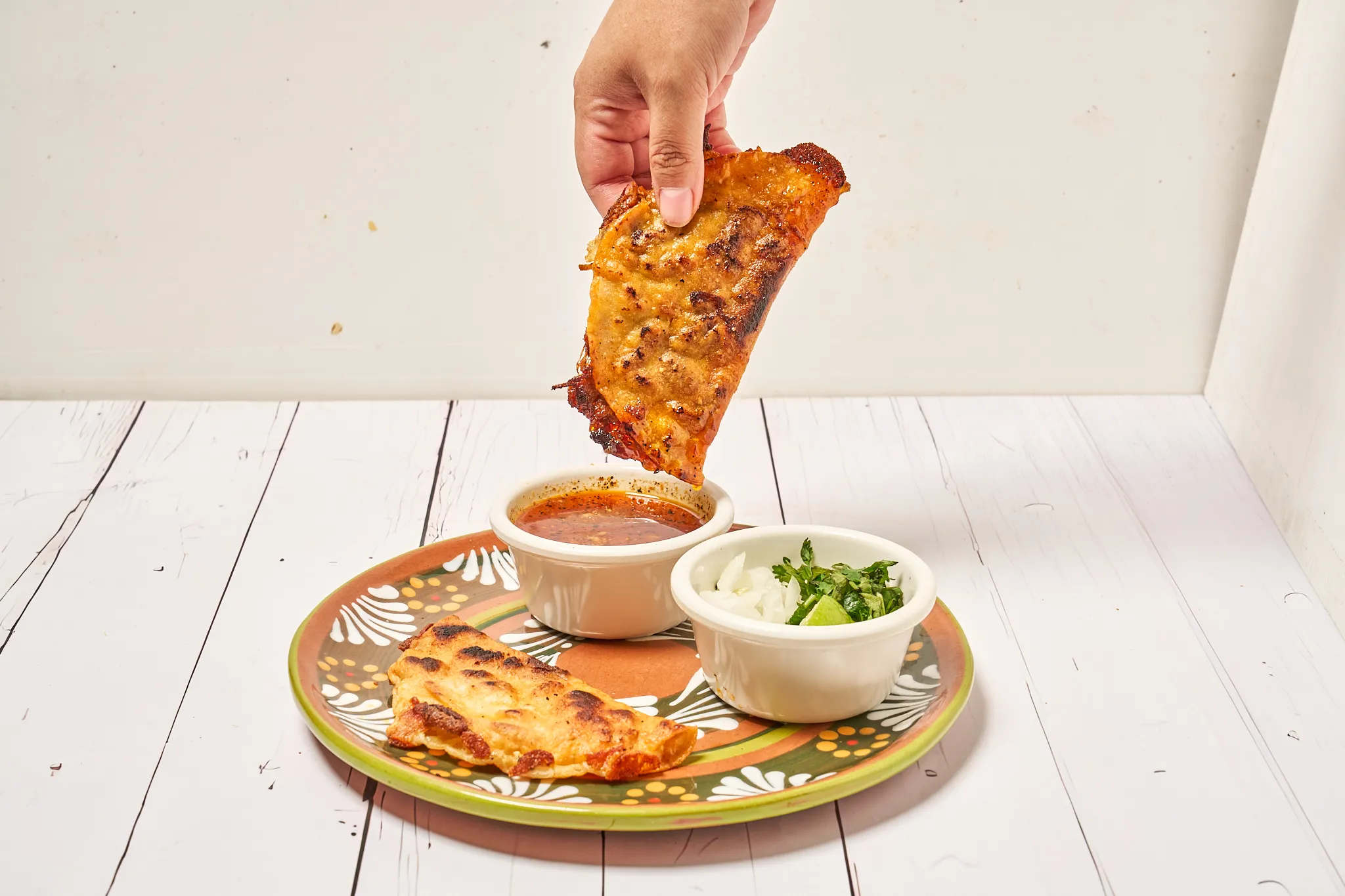 A hand dipping a quesabirria taco into consommé